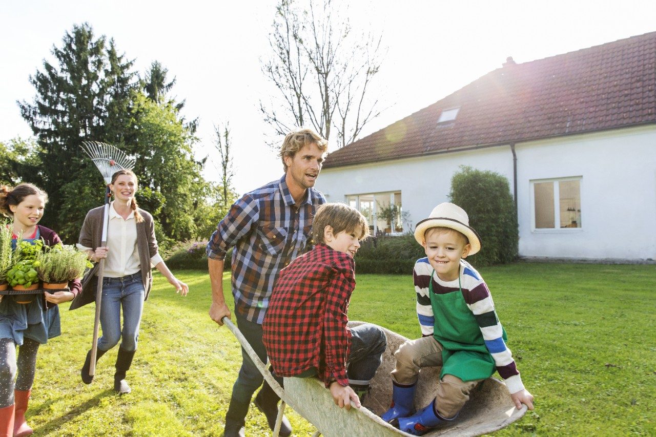 Man pushing two boys in wheelbarrow in front of single family house