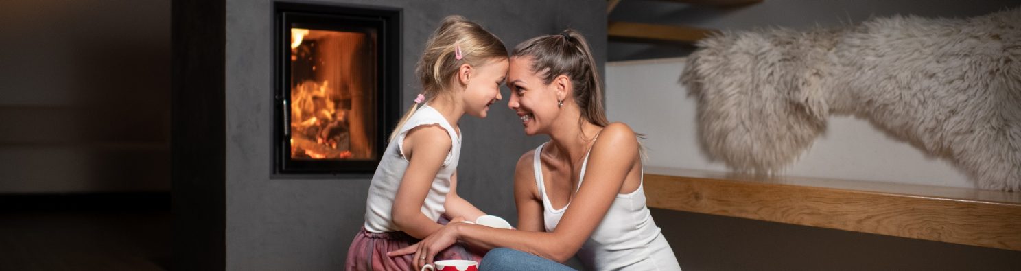 Žena maminka sedící s dítětem u teplého krbu v popředí cihla Porotherm T Profi
